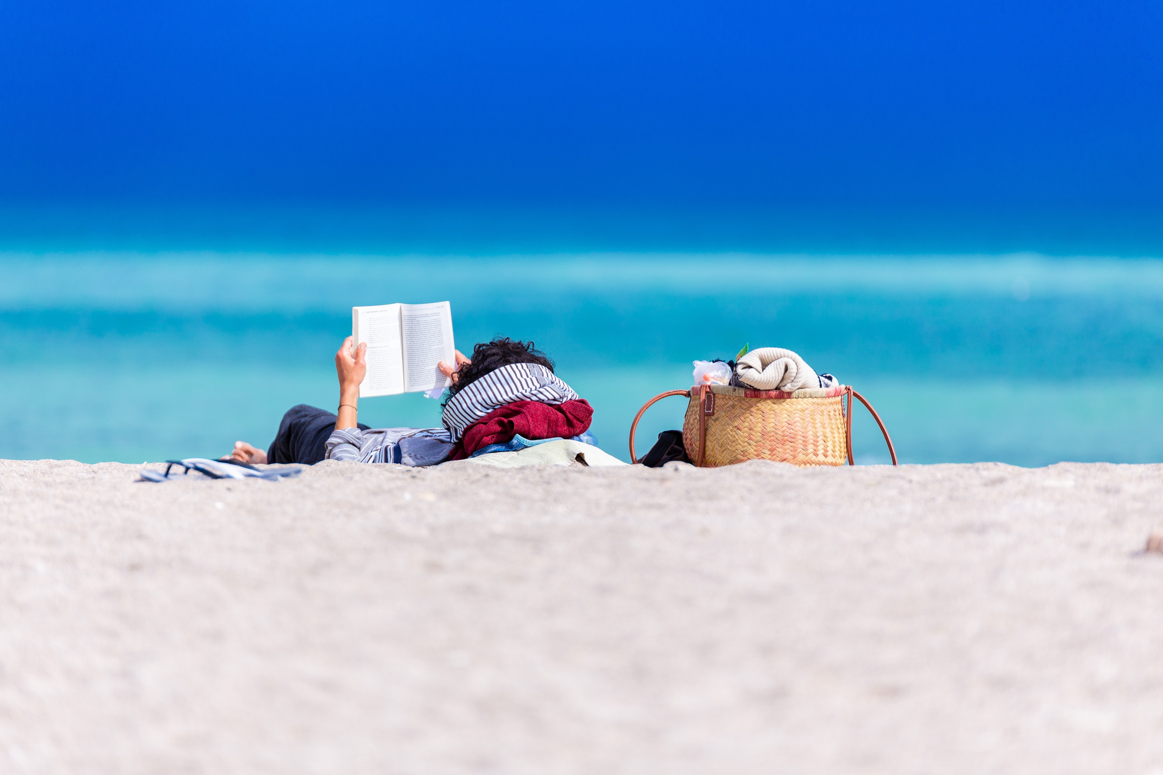 Reading by the beach near clear blue water and sky